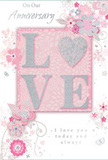 Captured as though propped on a mantle in a Fulham home, this anniversary card radiates a gentle, intimate charm. The design centres on the word LOVE, its letters raised from the surface and coated with fine glitter in soft pink and silvery tones. The glitter creates a light-catching texture, suggesting a touch that is both smooth and faintly grainy, like decorative sugar on a celebration cake. This central word is set on a blush-pink panel, which subtly distinguishes it from the rest of the card and draws the eye inward. Flowing out from around the panel, a cascade of stylised flowers and slender leaves arcs gracefully across the surface. The blossoms are illustrated with thin, precise lines and shaded washes of blush, ivory, and dove grey, with delicate silver highlights that lend them a quiet sparkle. They twist and curl in loose, organic trails, reminiscent of the way a florist might let foliage tumble naturally from a bouquet prepared for delivery near Eel Brook Common or along Fulham Road. The background is a soft pastel pink, unhurried and open, giving space to the intricate floral detailing. Elegant script wording delivers anniversary messages and affirmations of enduring love, the handwriting-style font adding a note of sincerity and intimacy. Altogether, the card feels like a paper interpretation of a romantic floral arrangement-light, airy, and thoughtfully composed-perfect to pair with fresh anniversary flowers arriving the same day across Fulham, Chelsea, and nearby neighbourhoods.